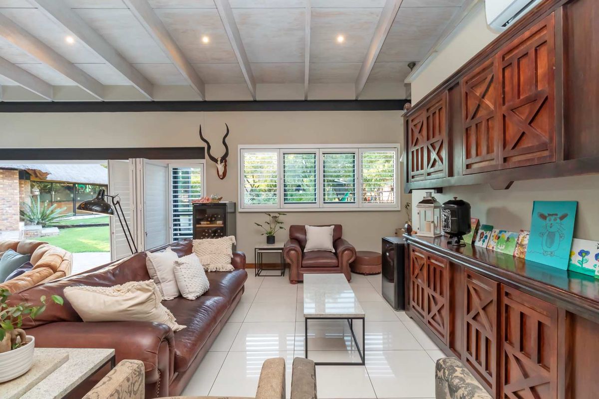 Spacious living room featuring high exposed beam ceilings, large white floor tiles, and custom built-in wooden cabinetry with direct access to the garden.