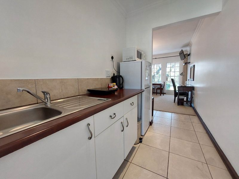A compact kitchen area featuring white cabinetry, a stainless steel sink, and tiled flooring, leading into an adjacent living space.
