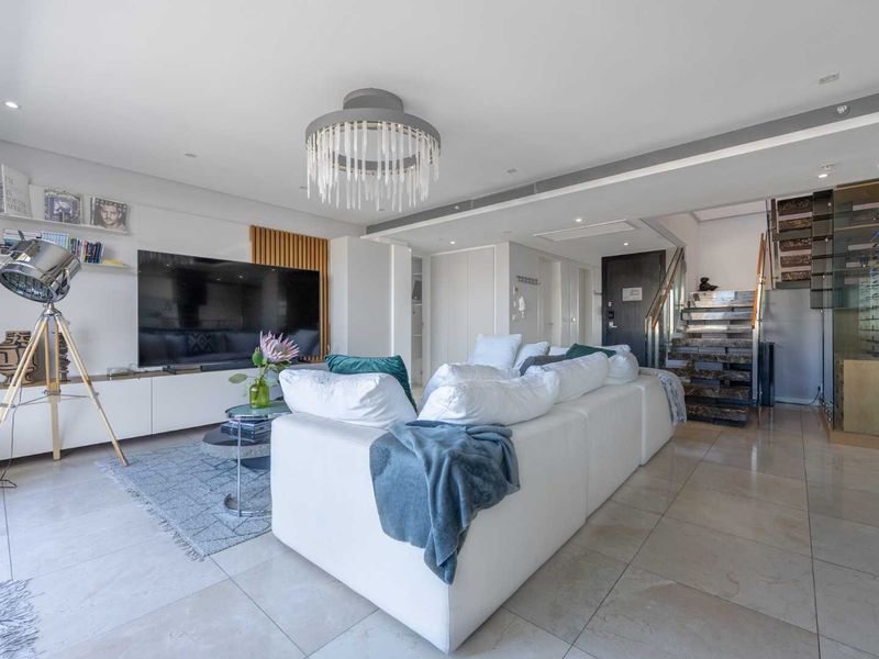 Modern open-plan living area featuring stone flooring, built-in cabinetry, a feature staircase with glass balustrade, and a dedicated wine display cabinet.