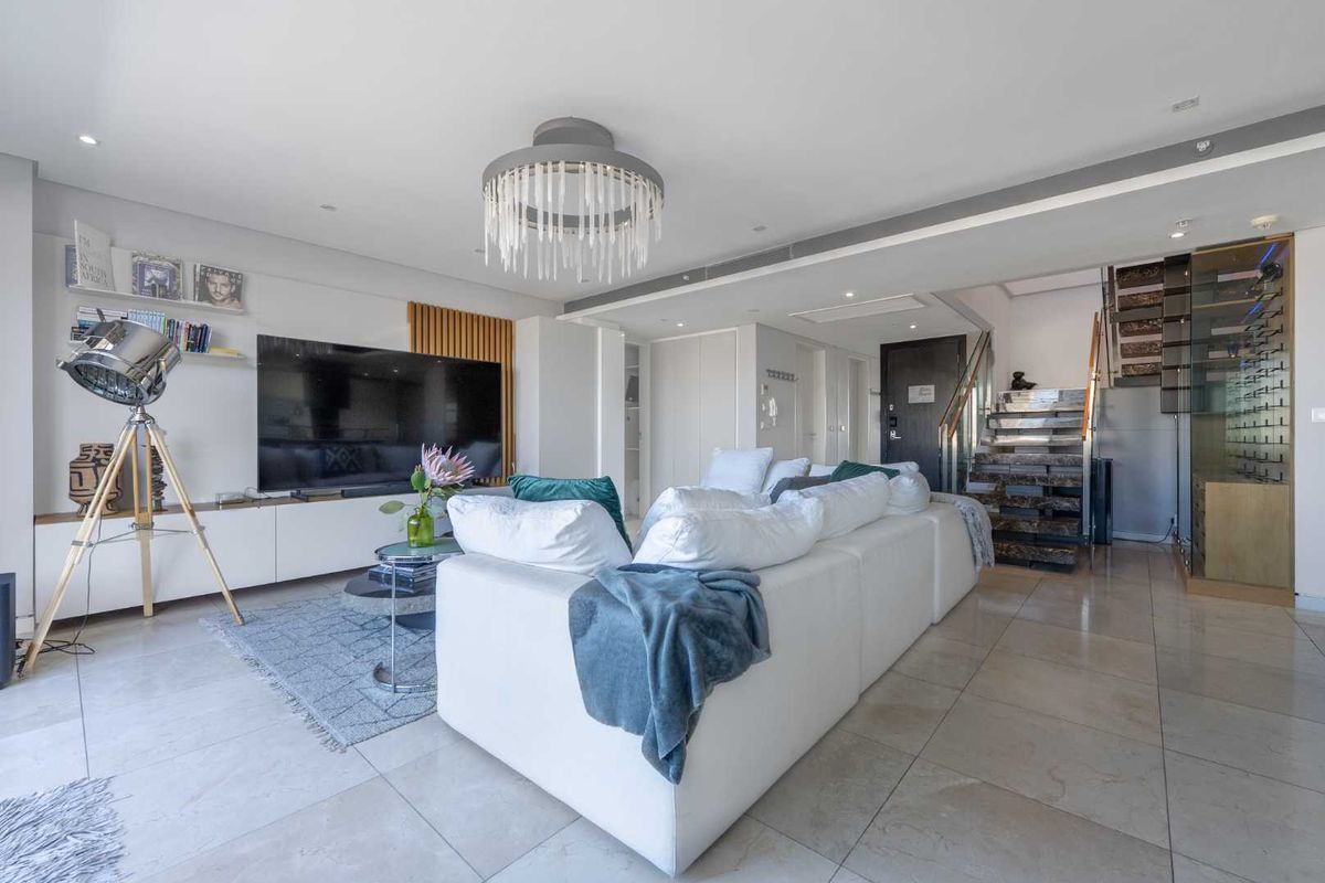 Modern open-plan living area featuring stone flooring, built-in cabinetry, a feature staircase with glass balustrade, and a dedicated wine display cabinet.