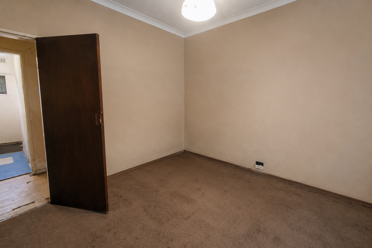 An empty bedroom featuring neutral walls, brown carpeting, and a classic wooden door, offering a blank canvas for renovation or restyling.