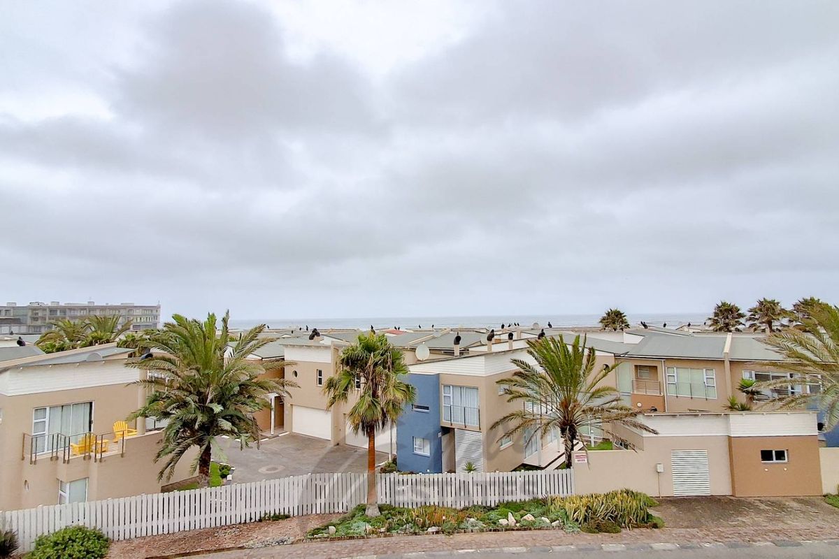 An elevated aerial view of a residential complex featuring multiple townhouses, paved driveways, and landscaped gardens with palm trees under a cloudy sky.