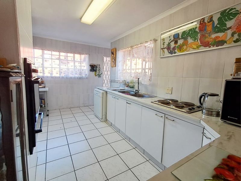 A functional kitchen featuring white cabinetry, tiled surfaces, a built-in oven, and an electric hob, offering a dated but practical layout.