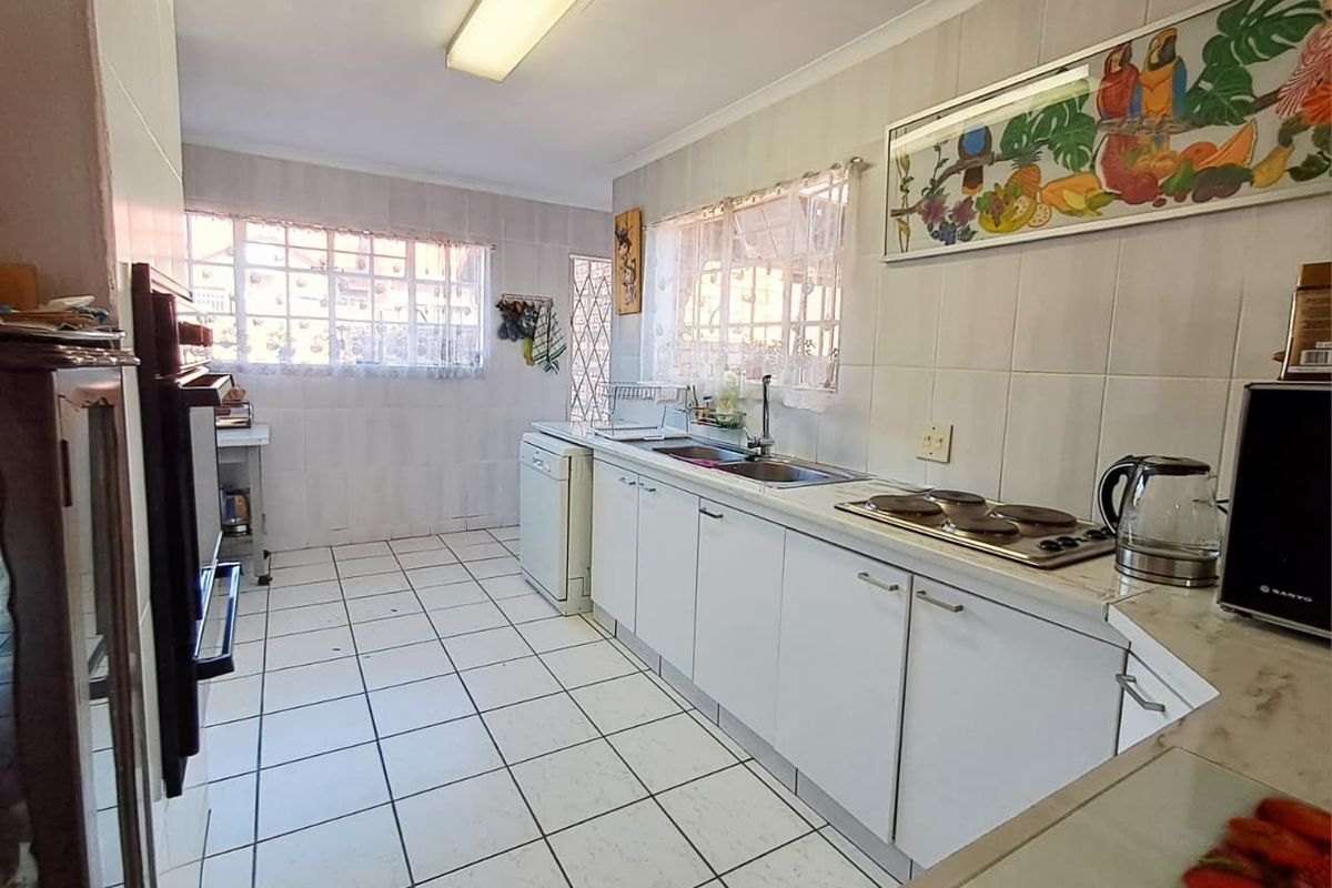 A functional kitchen featuring white cabinetry, tiled surfaces, a built-in oven, and an electric hob, offering a dated but practical layout.
