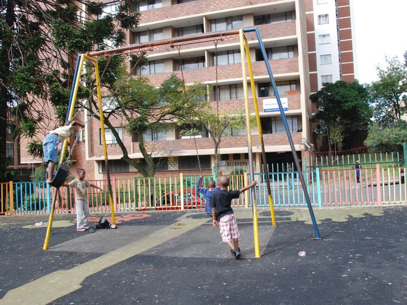 Outdoor playground area featuring a swing set and rubberized flooring, situated within a residential apartment complex.
