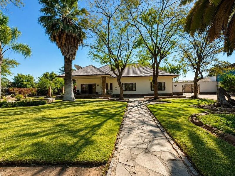 A well-maintained single-story house featuring a stone-paved walkway leading to the entrance, surrounded by a lush, landscaped garden with mature trees.