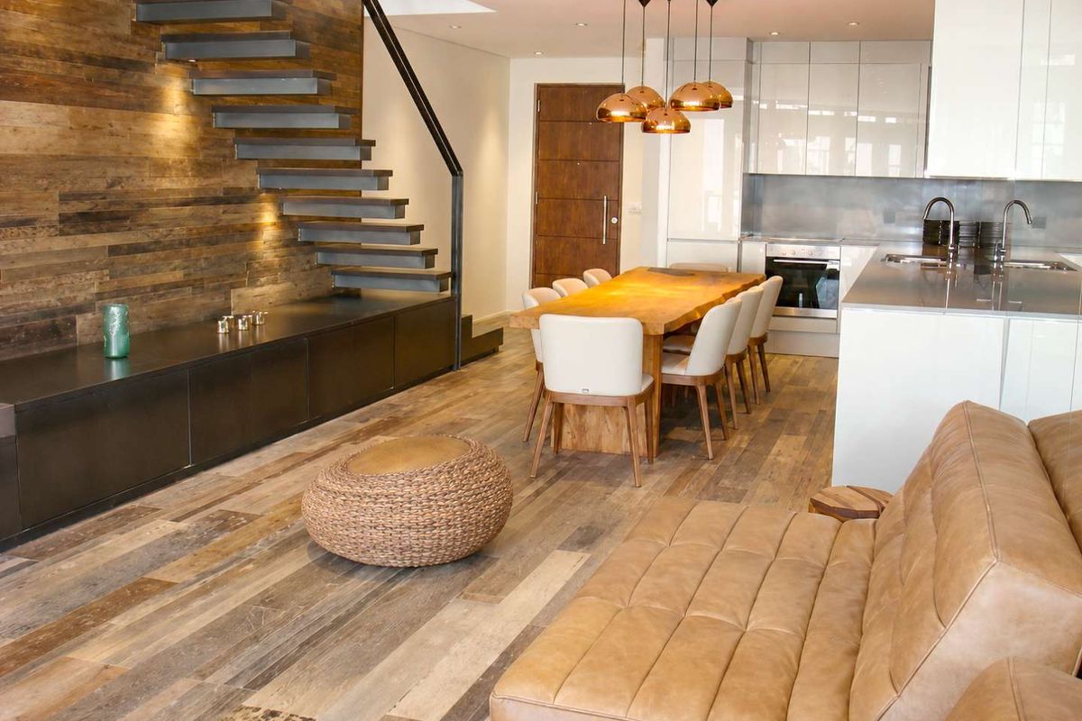 Modern open-plan living area featuring a striking floating staircase, timber wall cladding, and a sleek kitchen with integrated appliances and high-end finishes.