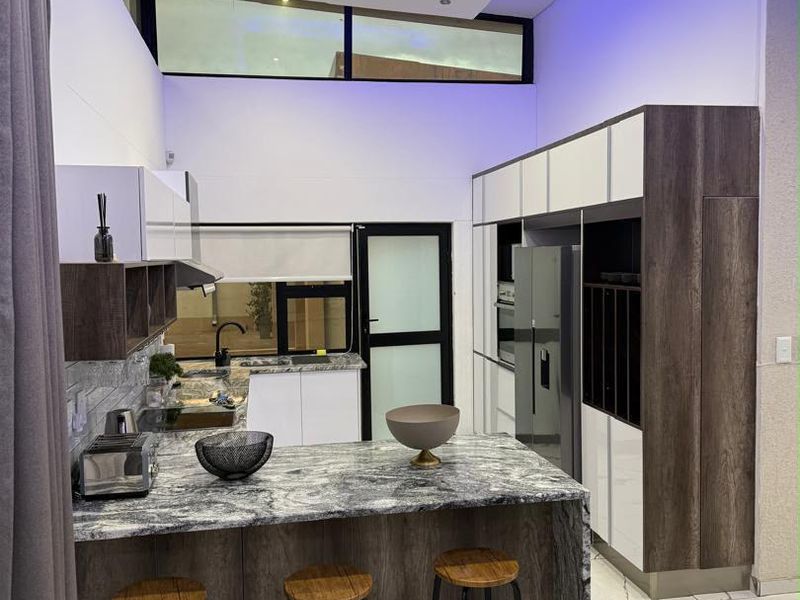 Modern kitchen featuring stone countertops, integrated appliances, sleek cabinetry, and high-contrast finishes with ambient recessed ceiling lighting.