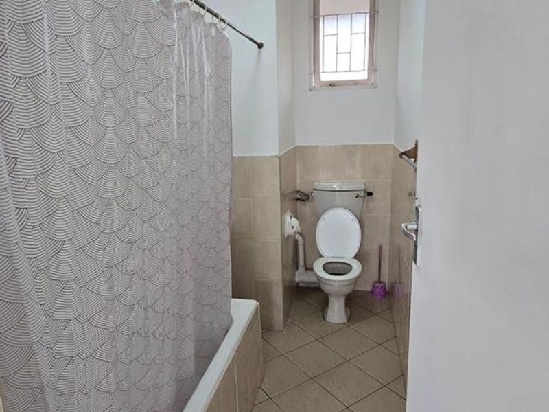 A functional bathroom featuring a bathtub with a shower curtain rail, a standard toilet, and neutral tiled finishes throughout.