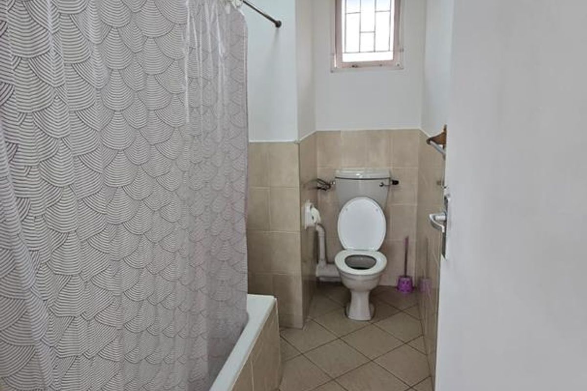 A functional bathroom featuring a bathtub with a shower curtain rail, a standard toilet, and neutral tiled finishes throughout.