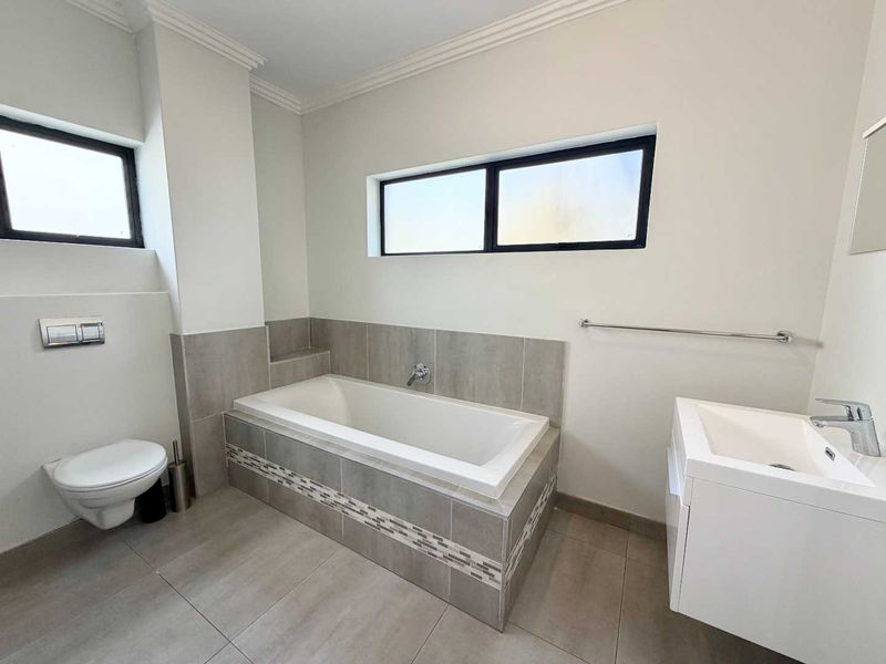 A clean, modern bathroom featuring a wall-hung toilet, a built-in bathtub with tiled surround, and a contemporary vanity basin.