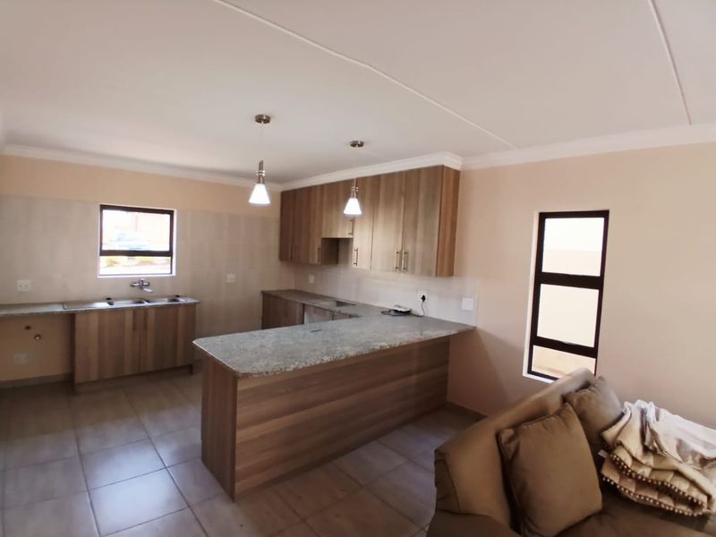 Modern open-plan kitchen featuring wood-finish cabinetry, granite countertops, a functional island, and tiled flooring, seamlessly integrated with the living area.