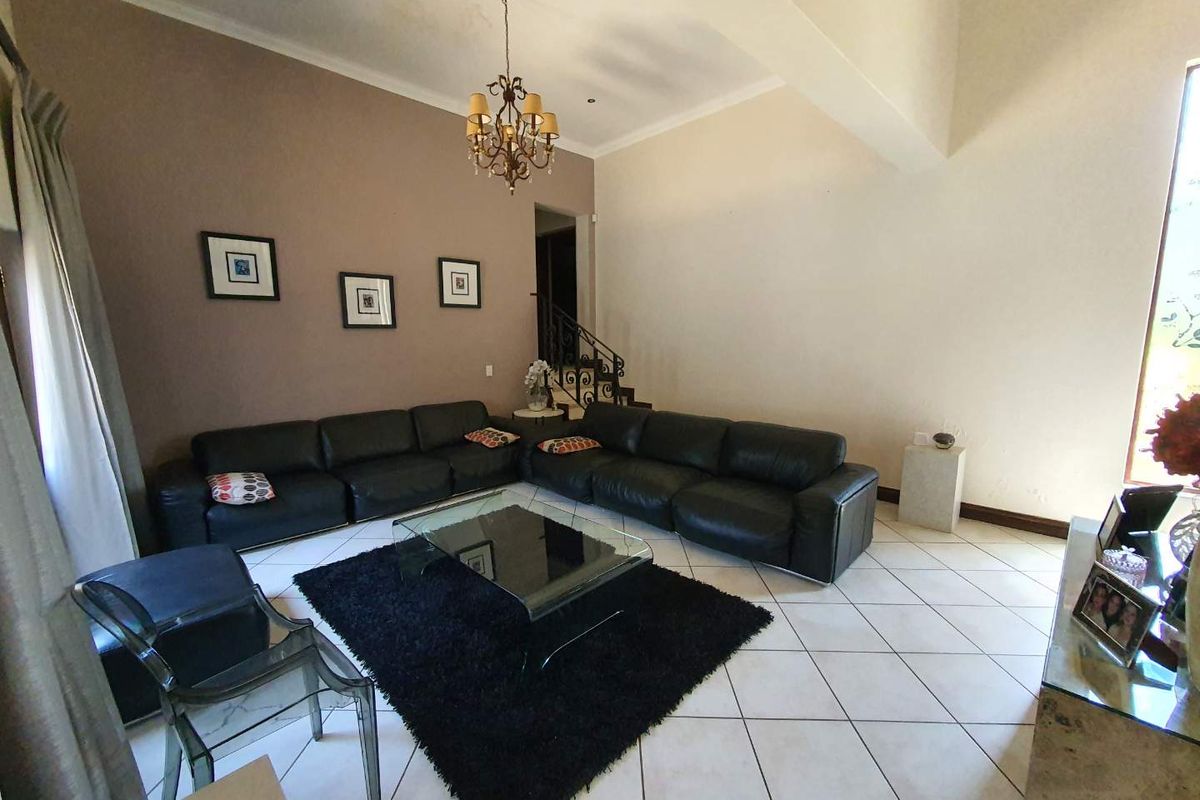Spacious living room featuring tiled flooring, a vaulted ceiling with a chandelier, and an open staircase with wrought iron railings.
