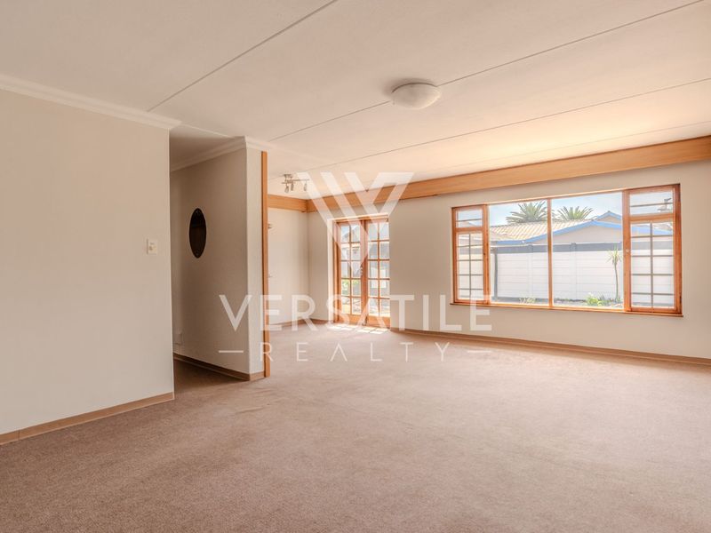 A spacious, empty living room featuring neutral carpeting, timber-framed windows, and french doors leading to the exterior.
