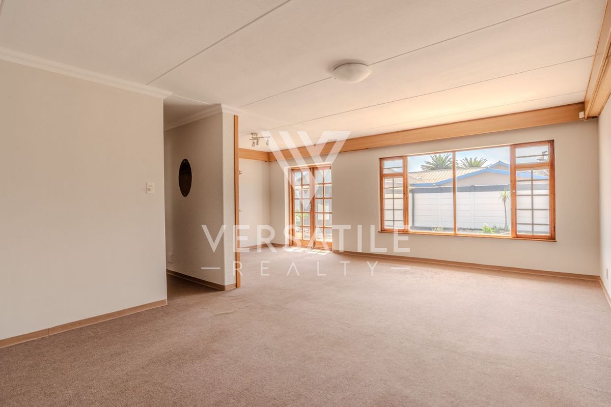 A spacious, empty living room featuring neutral carpeting, timber-framed windows, and french doors leading to the exterior.