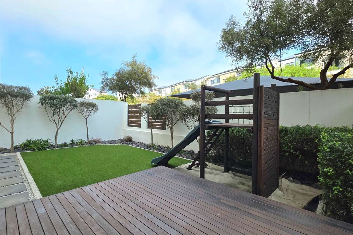 A well-maintained rear garden featuring timber decking, artificial lawn, and a secure boundary wall with privacy screening.