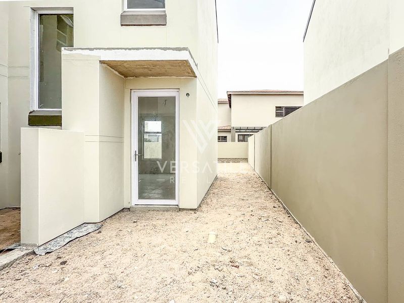Rear exterior view of the townhouse featuring a gravel courtyard, boundary wall, and a glass panel door leading into the home.
