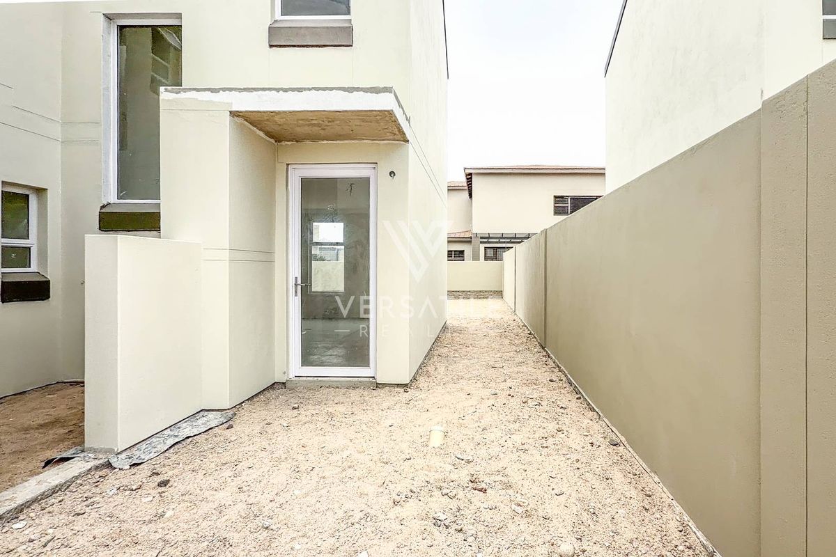 Rear exterior view of the townhouse featuring a gravel courtyard, boundary wall, and a glass panel door leading into the home.