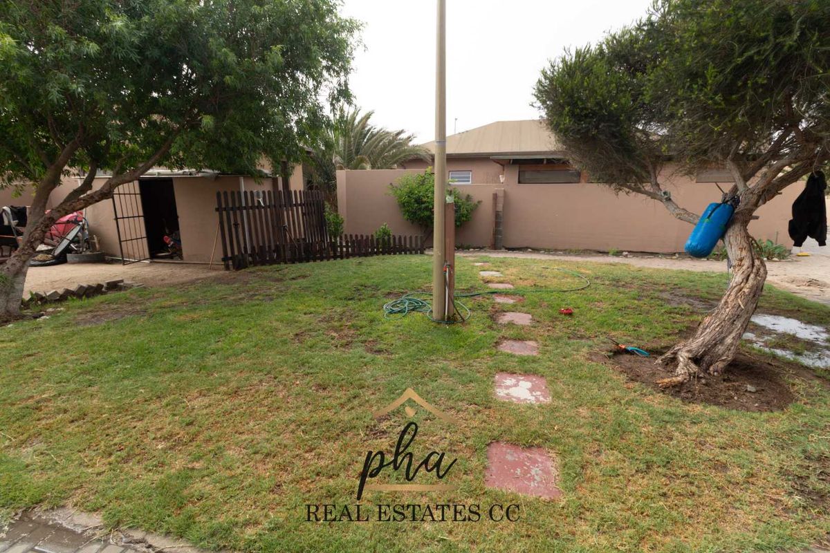 A rear garden area featuring a lawn, a stone pathway, a boundary wall, and a small utility shed.