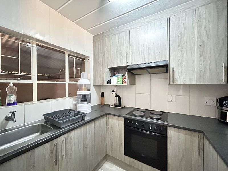 A functional kitchen featuring light wood-grain cabinetry, dark countertops, a built-in electric oven and hob, and a tiled backsplash.