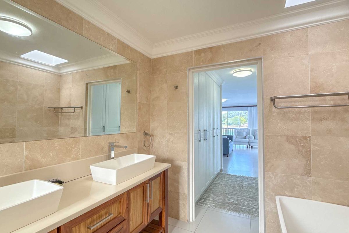 A well-appointed bathroom featuring a double vanity with vessel sinks, stone wall tiling, a large mirror, and a separate bathtub.