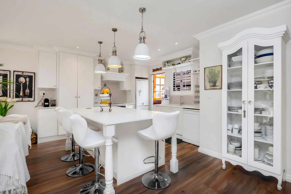 Bright, modern kitchen featuring a central island with breakfast bar seating, white cabinetry, integrated appliances, and warm wood-look flooring.