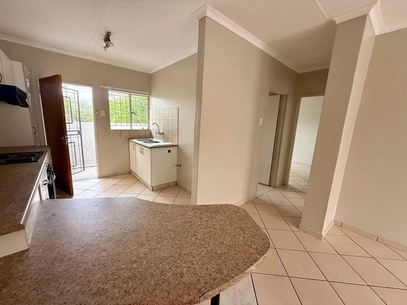 A functional kitchen area featuring tiled flooring, laminate countertops, and direct access to an exterior space through a security gate.