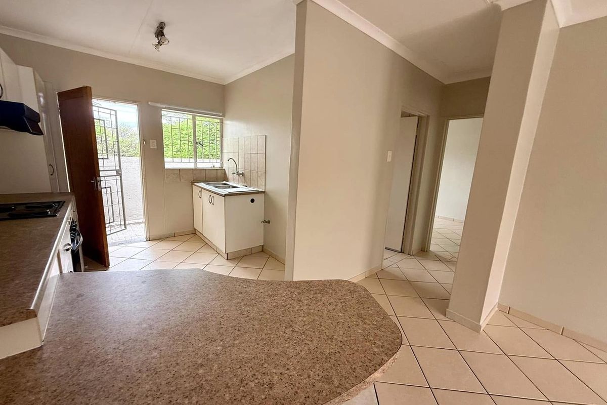 A functional kitchen area featuring tiled flooring, laminate countertops, and direct access to an exterior space through a security gate.