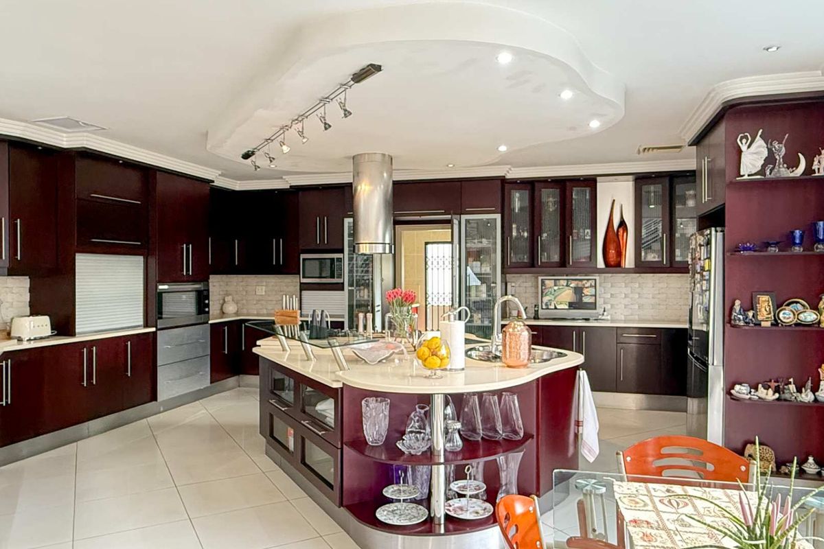 Spacious kitchen featuring dark cabinetry, a central island with integrated sink, stone countertops, and a distinctive recessed ceiling with spotlighting.