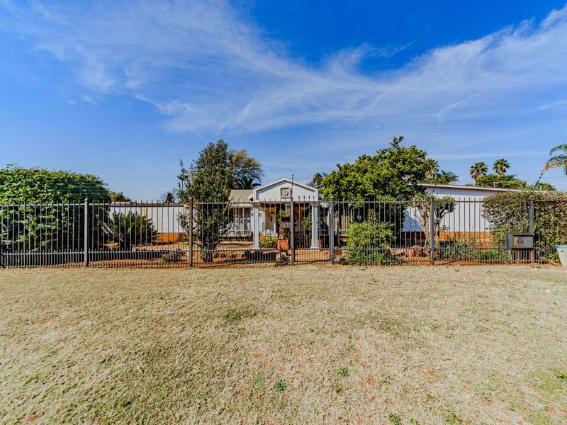 Front view of the property featuring a large lawn, secure metal perimeter fencing, and a gated entrance leading to the main residence.