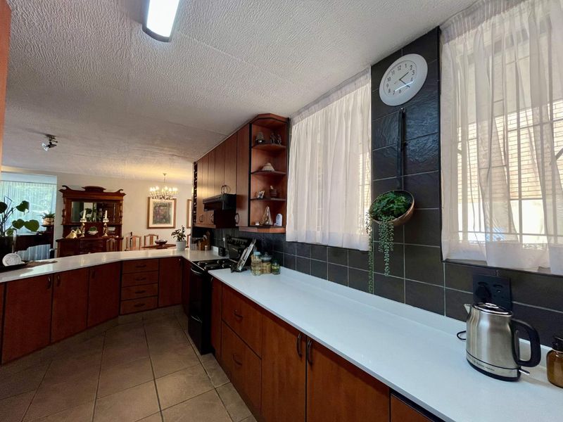 A functional kitchen featuring dark wood cabinetry, white countertops, and dark tiled splashbacks, flowing into an adjacent dining area.