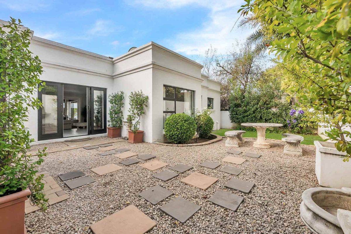 A private rear garden featuring a gravel courtyard, stone paver pathway, and direct access to the home through large sliding glass doors.