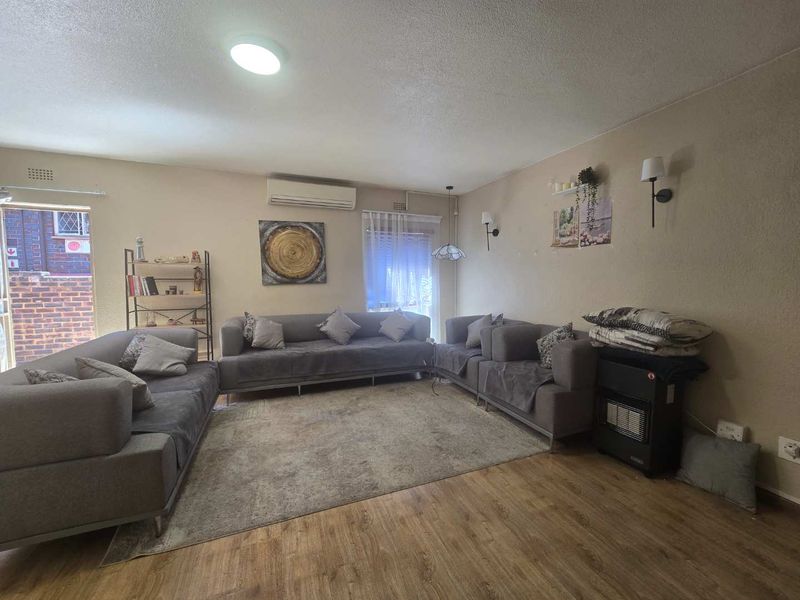 Spacious living room featuring laminate flooring, wall-mounted lighting, and an air conditioning unit, offering a comfortable and functional living space.