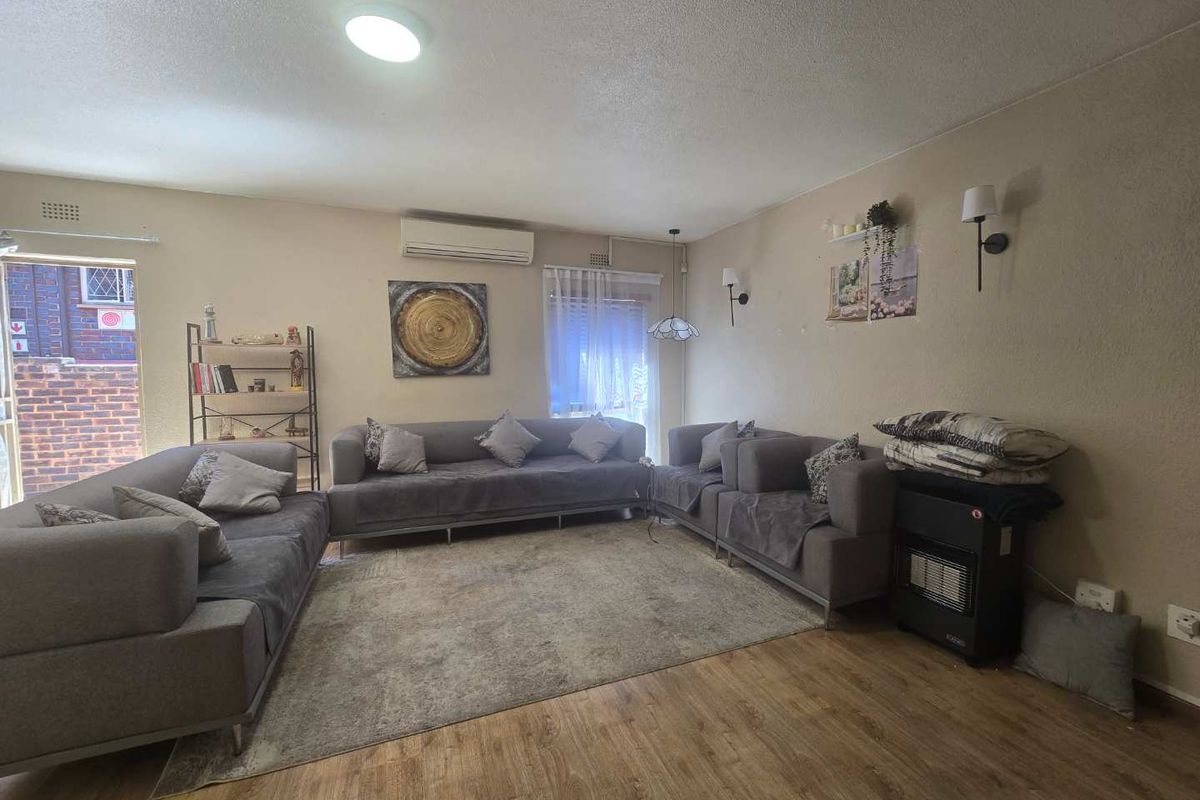 Spacious living room featuring laminate flooring, wall-mounted lighting, and an air conditioning unit, offering a comfortable and functional living space.