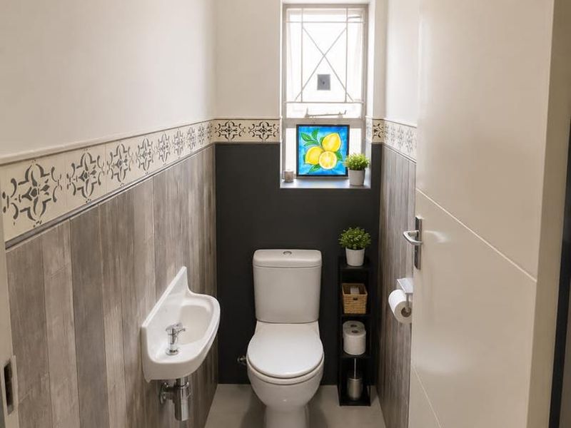 A compact, well-maintained guest bathroom featuring a wall-mounted basin, modern toilet, and stylish half-height tiled walls with a decorative border.