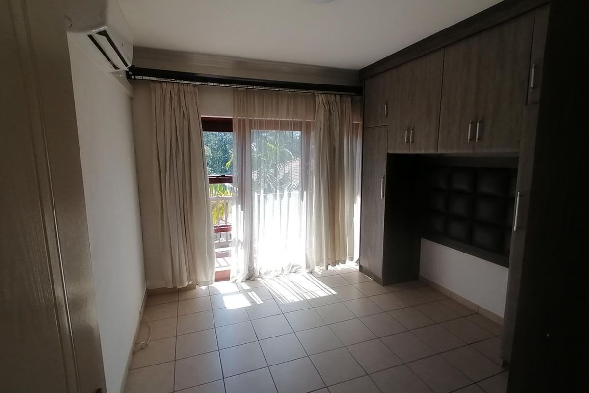A bright, empty bedroom featuring tiled floors, built-in cupboards with an integrated headboard, and a sliding door leading to an outdoor area.