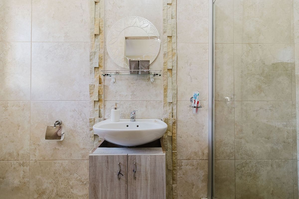 A bathroom featuring stone-tiled walls, a vanity cabinet with a ceramic basin, and a glass shower enclosure.