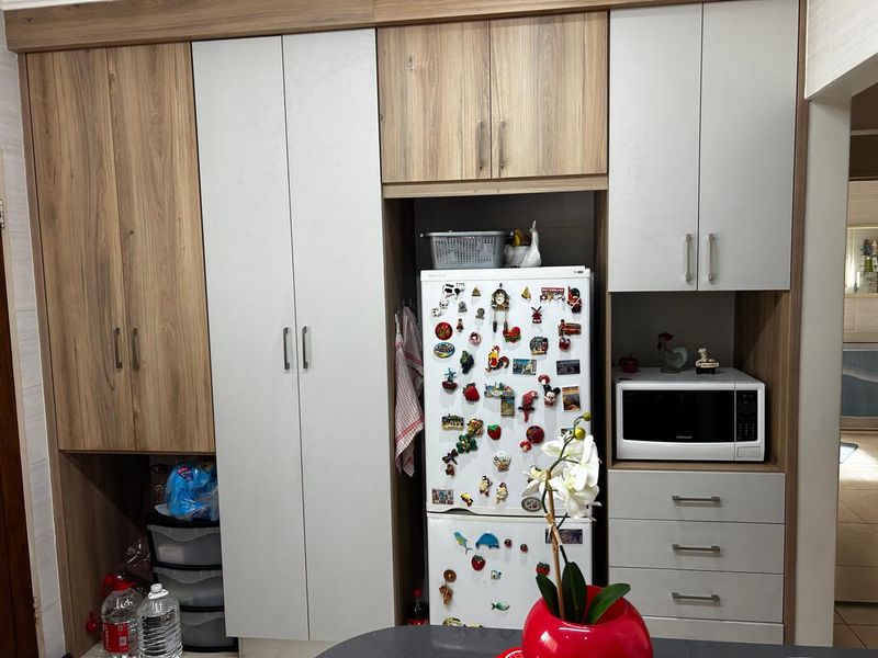 A functional kitchen wall featuring integrated cabinetry with a mix of wood-grain and matte white finishes, including dedicated space for a refrigerator and microwave.