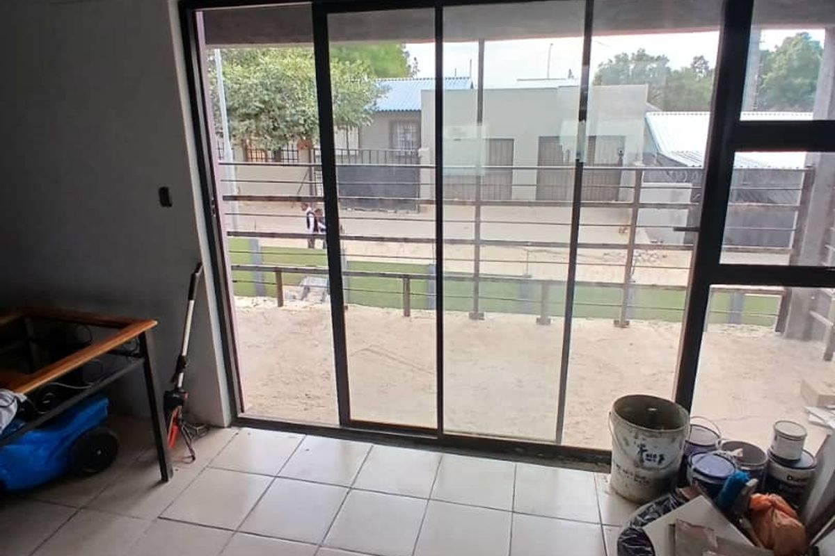 An empty living room featuring large sliding glass doors with security bars and ceramic tiled flooring, currently undergoing renovation or finishing work.