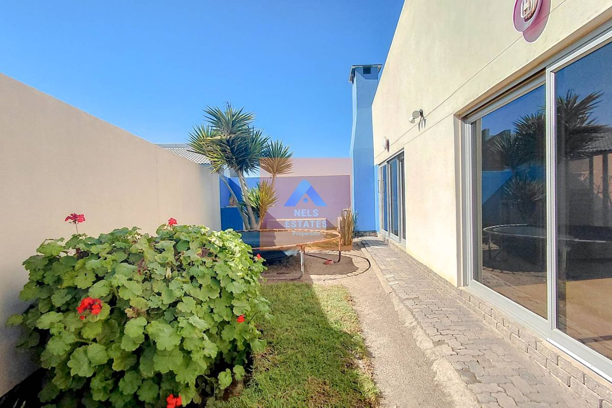 A private rear courtyard featuring a paved walkway, small lawn area, and direct access to the home through sliding glass doors.