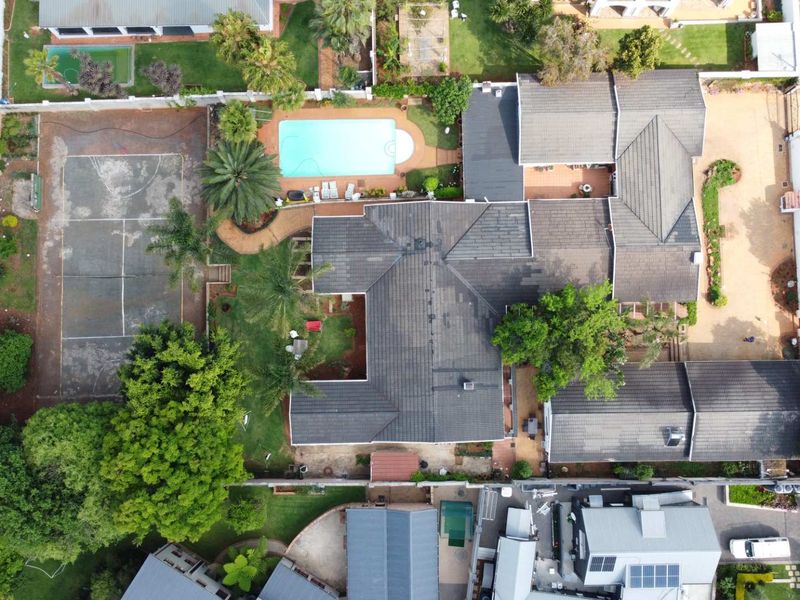 Aerial view of the property featuring a large tiled roof house, private swimming pool, tennis court, and established garden areas on a spacious lot.
