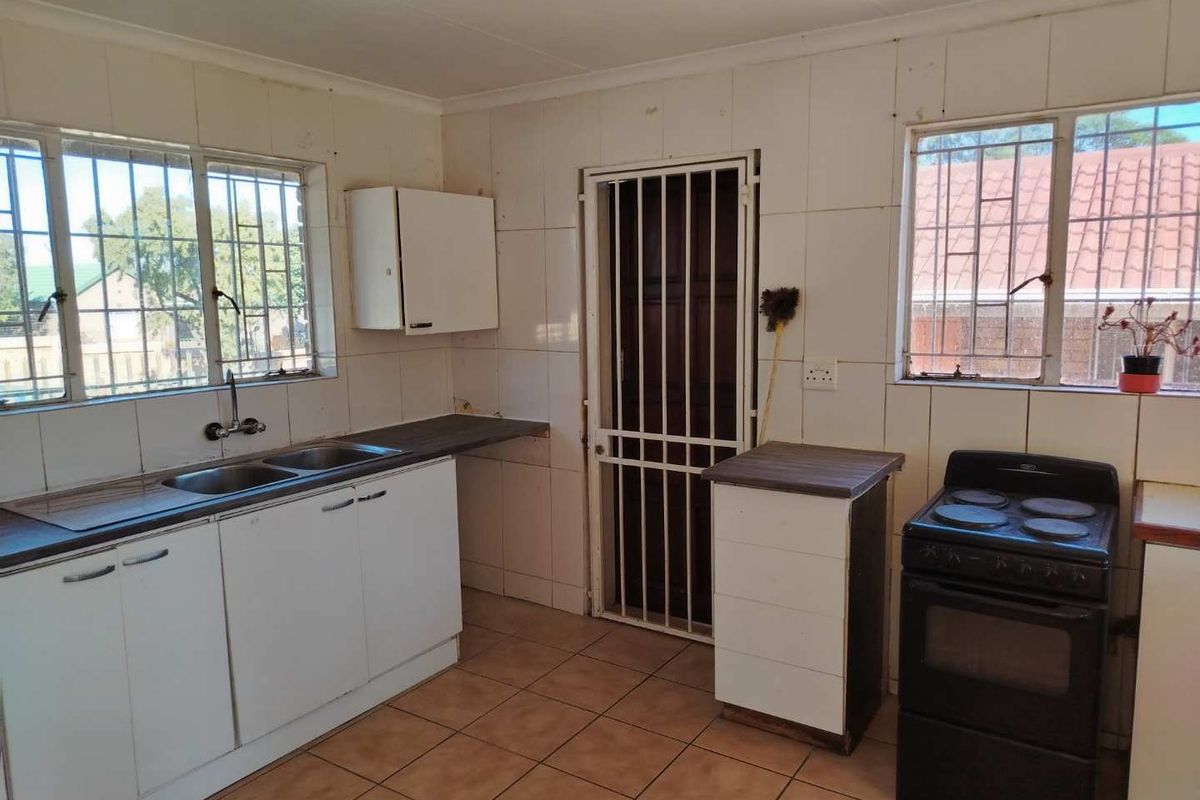 A functional kitchen featuring tiled walls and flooring, double sink, and built-in cabinetry, offering potential for modernization and cosmetic updates.