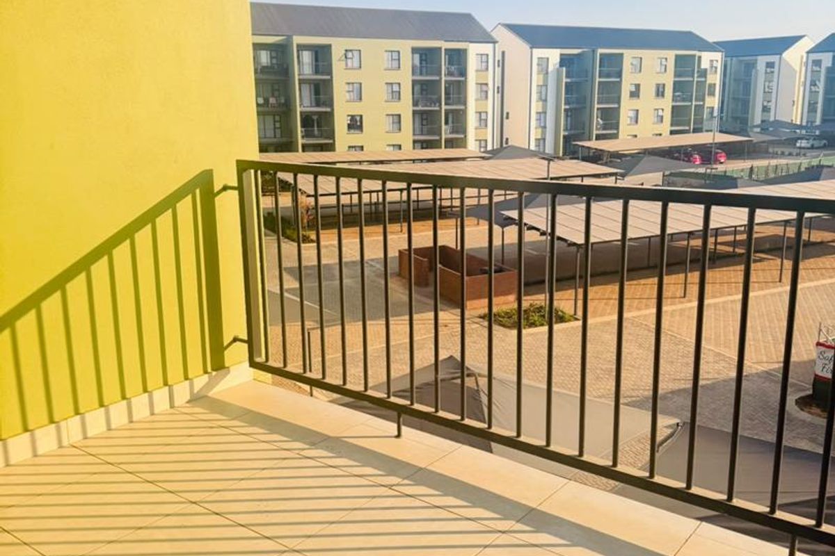 A clean, tiled balcony featuring a metal balustrade with views over the apartment complex grounds and parking area.