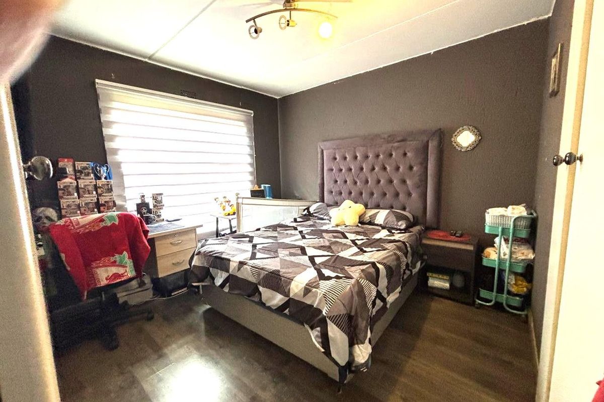A bedroom featuring dark-toned walls, wood-look flooring, a window with fitted blinds, and a ceiling-mounted light fixture.