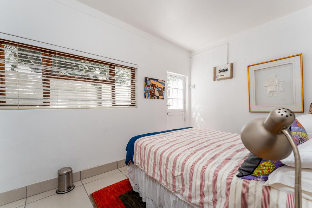 A bright bedroom featuring tiled flooring, a large window with horizontal blinds, and a private exterior access door.
