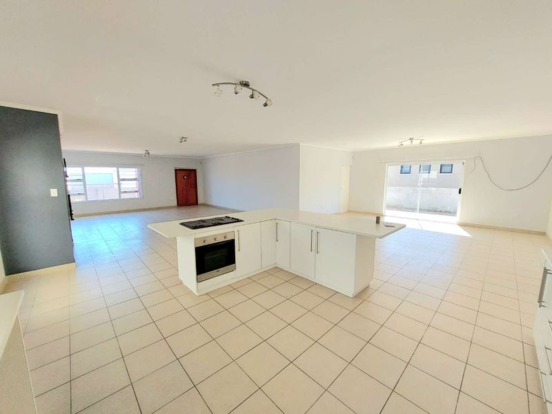 Spacious open-plan living area featuring a central kitchen island with built-in oven and hob, tiled flooring, and large sliding doors leading outdoors.