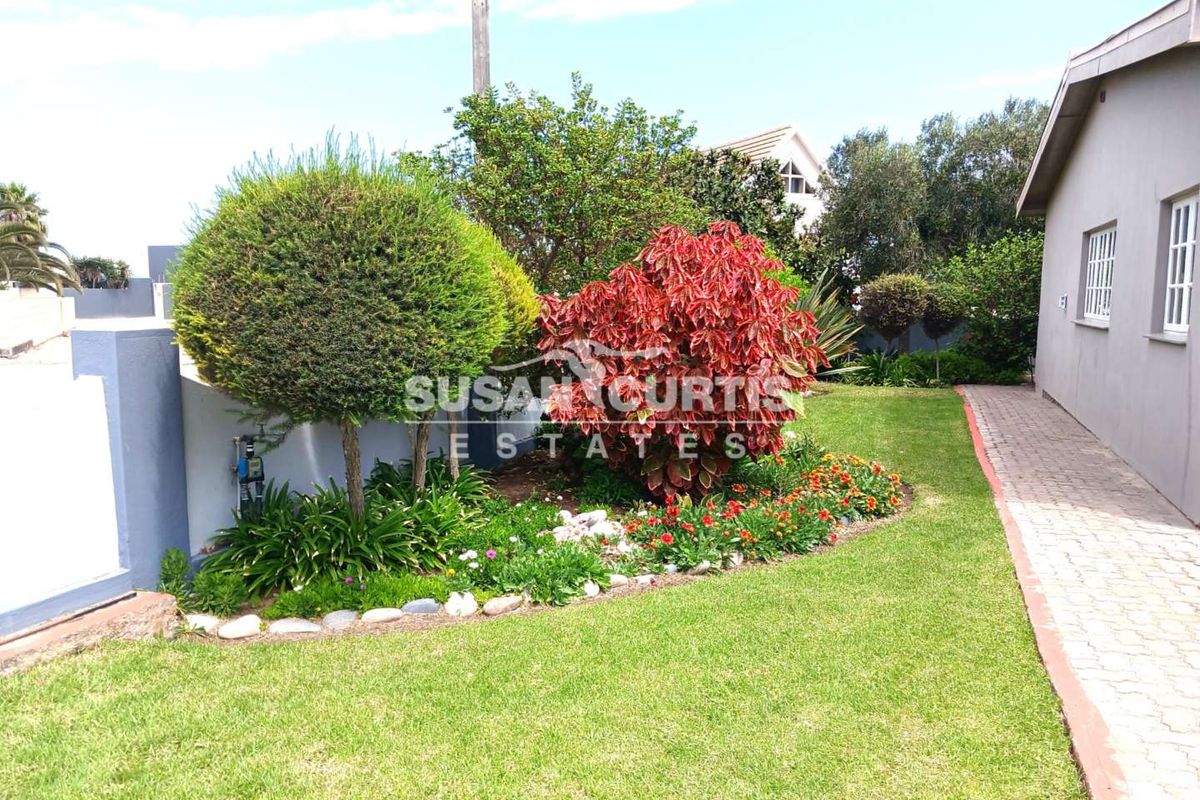 A well-maintained rear garden area featuring a manicured lawn, landscaped flower beds, and a paved walkway alongside the exterior wall of the house.