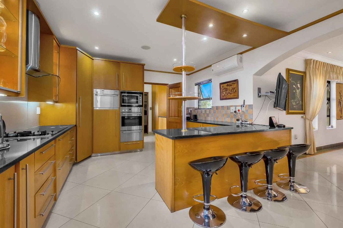 Spacious kitchen featuring warm-toned wooden cabinetry, dark granite countertops, built-in oven and microwave, and a breakfast bar island with integrated lighting.