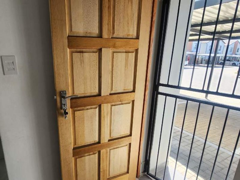 Entrance area featuring a solid timber panel door and a secure metal gate, leading out to a paved driveway area.