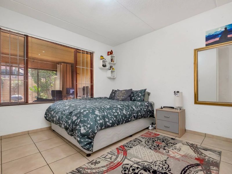 A well-lit bedroom featuring neutral tiled flooring and a large window with venetian blinds, offering a clean and functional living space.